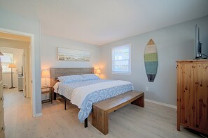 Un dormitorio con una cama, un banco de madera, una tabla de surf colgada en la pared y una ventana con persianas.