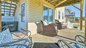 A covered outdoor area with wicker furniture, a trash bin, and a glass door leading to a building.