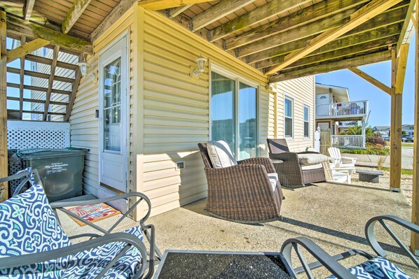 A covered outdoor area with wicker furniture, a trash bin, and a glass door leading to a building. - Coastal Brigantine Retreat - Walk to Beach! (Brigantine)