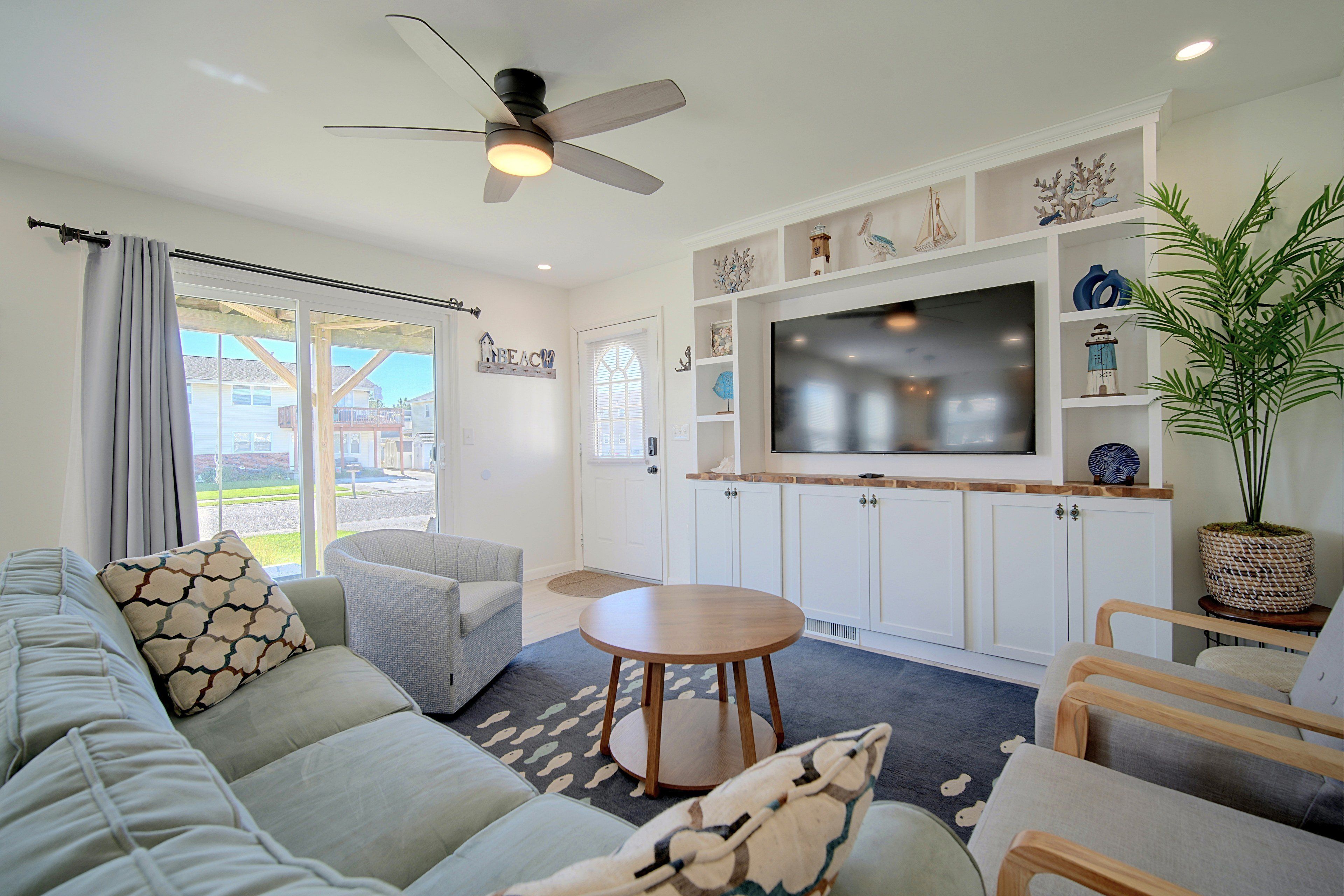 A modern living room with a sofa, armchairs, a TV, and a ceiling fan.