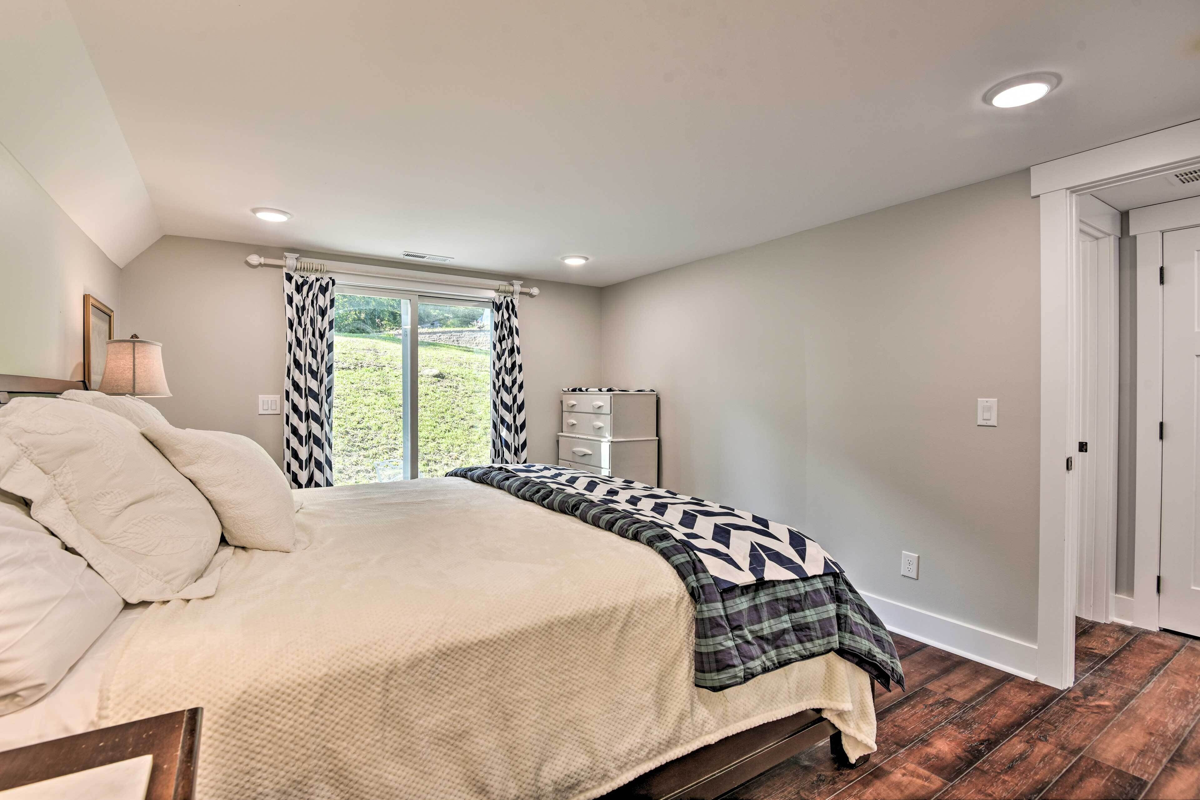 A bedroom with a bed, a dresser, a window with curtains, and a view of the outdoors.