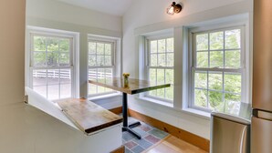 A kitchen with a wooden table, a refrigerator, and large windows with a view of greenery. - Quaint Goshen Apartment w/ Patio! (Goshen)