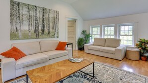 A spacious living room with two sofas, a coffee table, and a large painting of a forest. - Quaint Goshen Apartment w/ Patio! (Goshen)