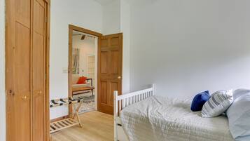 A bedroom with a wooden wardrobe, a bed with pillows, and a small table with a chair.