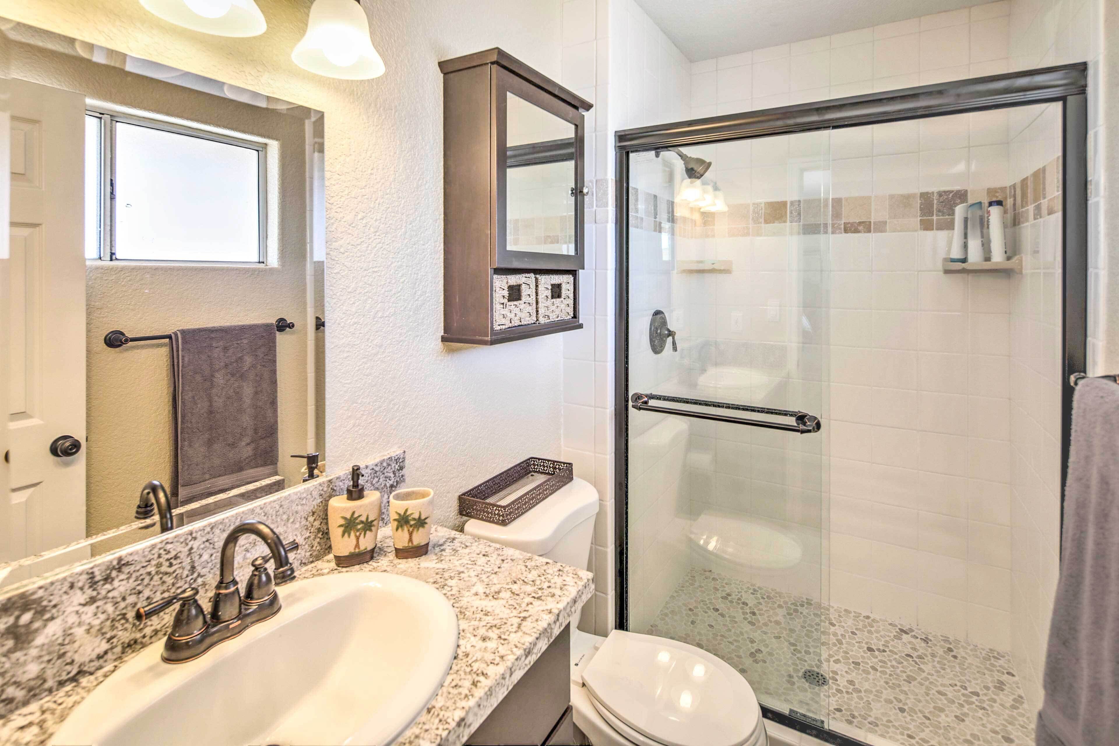 A bathroom with a granite countertop sink, a mirror, a toilet, and a glass-enclosed shower.