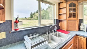 A kitchen with a double sink, wooden cabinets, and a window overlooking a grassy area.
