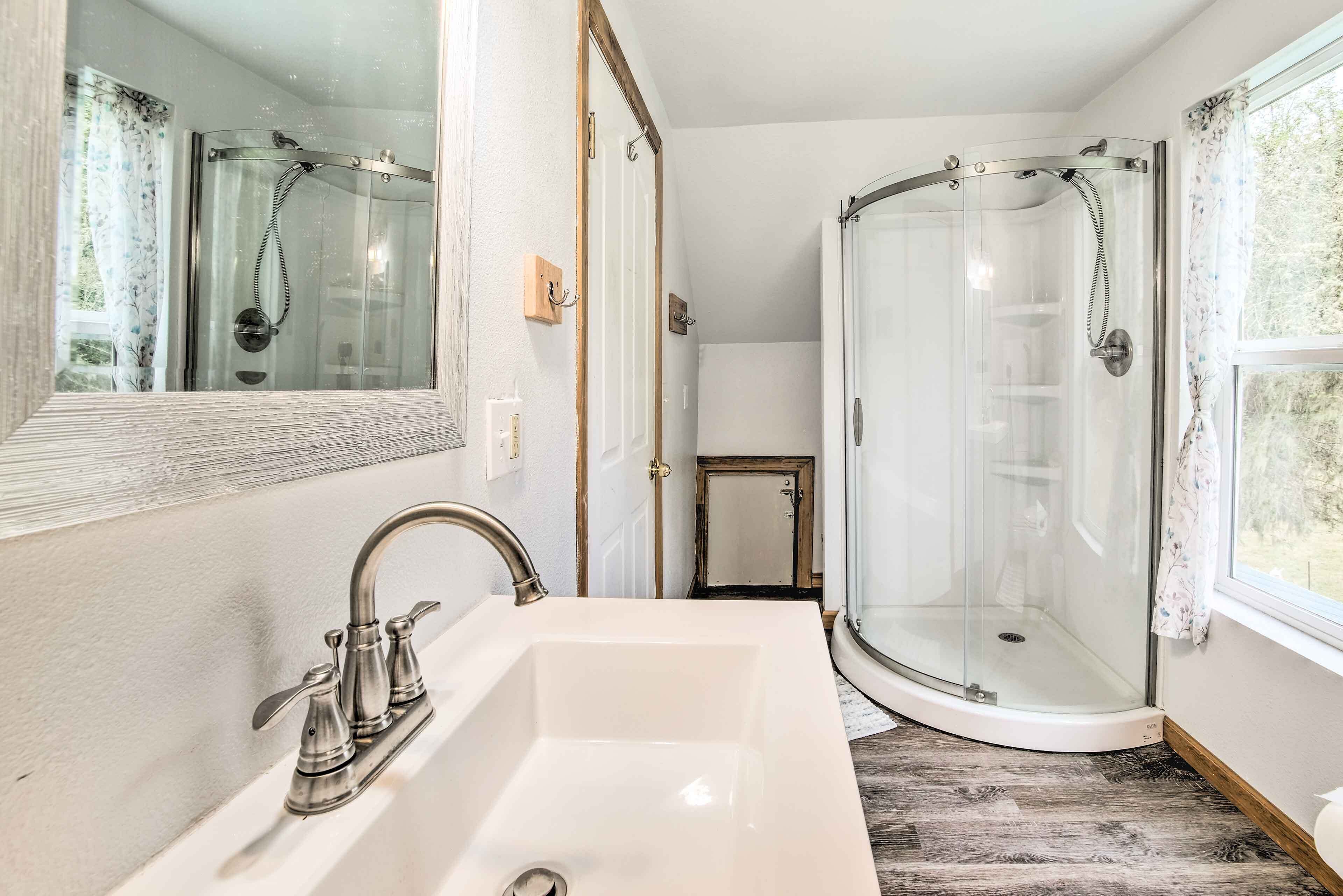Une salle de bain avec un lavabo blanc, une cabine de douche en verre et une fenêtre laissant entrer la lumière naturelle.