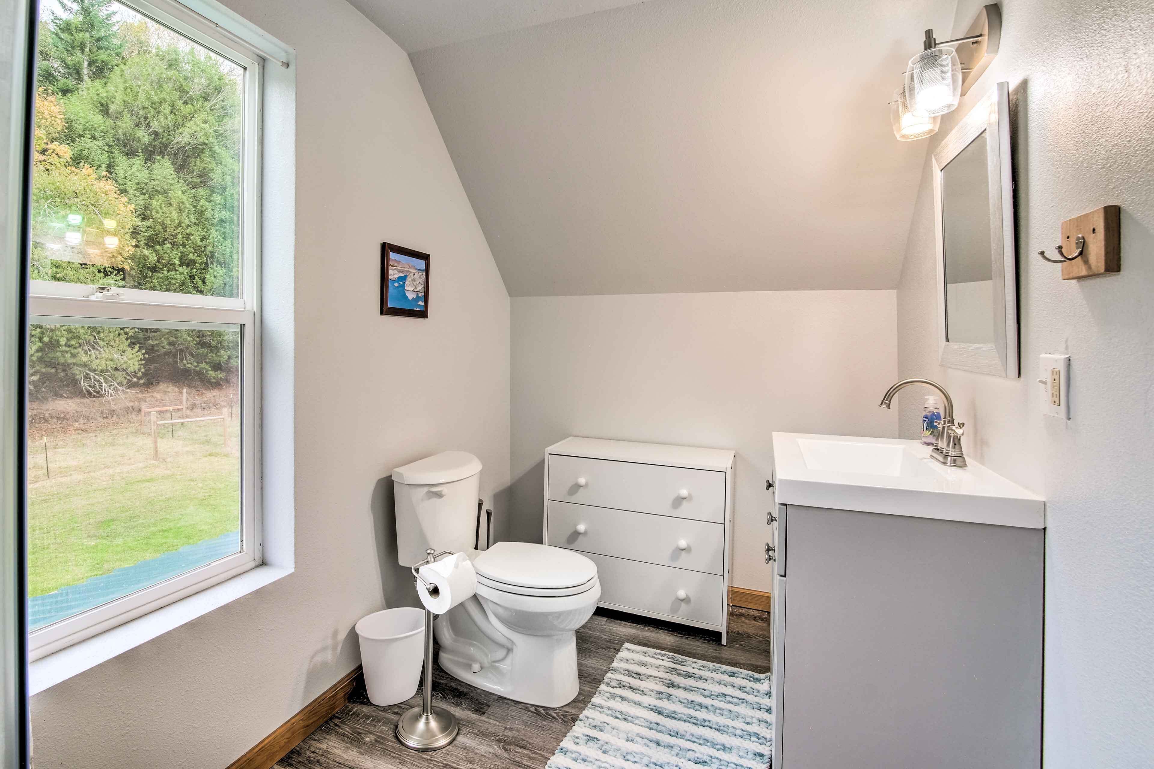 A bathroom with a toilet, sink, and a window with a view of a grassy area.