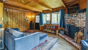 A cozy cabin interior with a wooden ceiling, a brick fireplace, a sofa, and a television mounted above it. - Groveland Vacation Rental ~ 24 Mi to Yosemite! (Groveland)