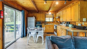 A wooden cabin interior with a dining area, kitchen, and a large sliding glass door leading to an outdoor deck. - Groveland Vacation Rental ~ 24 Mi to Yosemite! (Groveland)