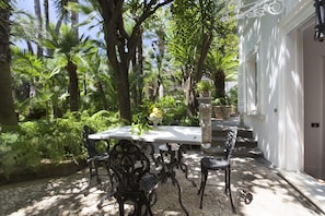 An outdoor patio with a table and chairs, surrounded by lush greenery and palm trees.