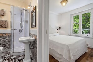 A bathroom with a shower, toilet, and sink. There is a bed with a window in the adjacent room. - Villa Le Camelie in Sant Agnello (Sant'Agnello)