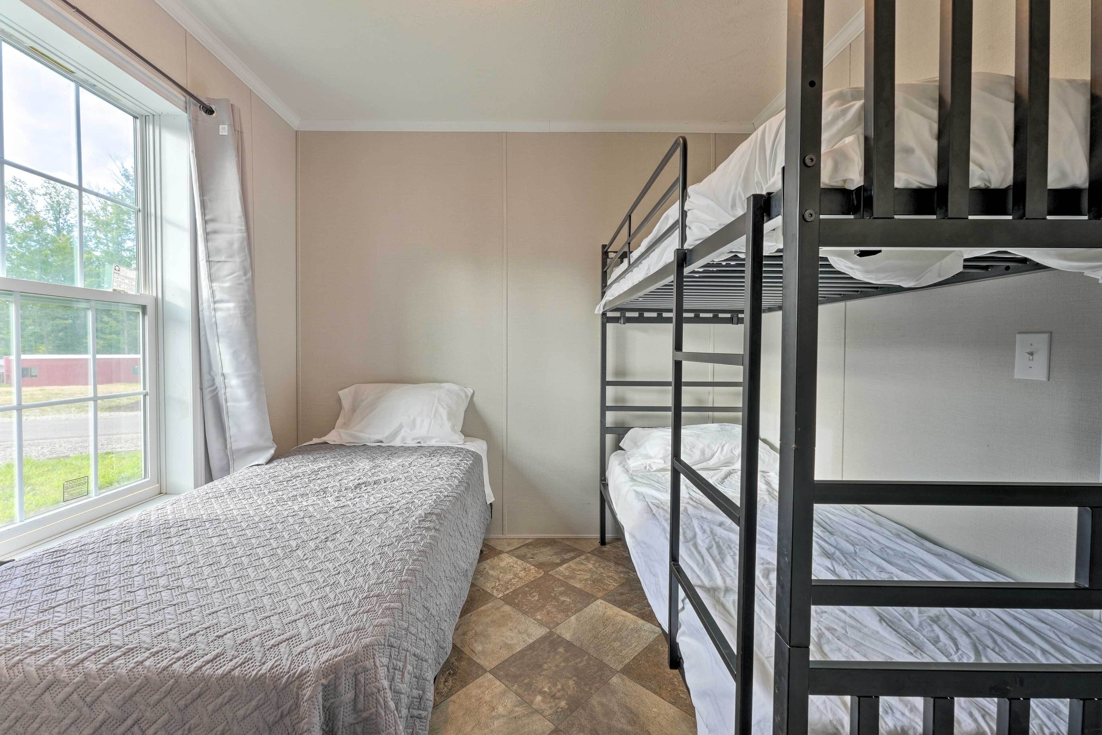A dormitory room with bunk beds, a single bed, a window with curtains, and a tiled floor.