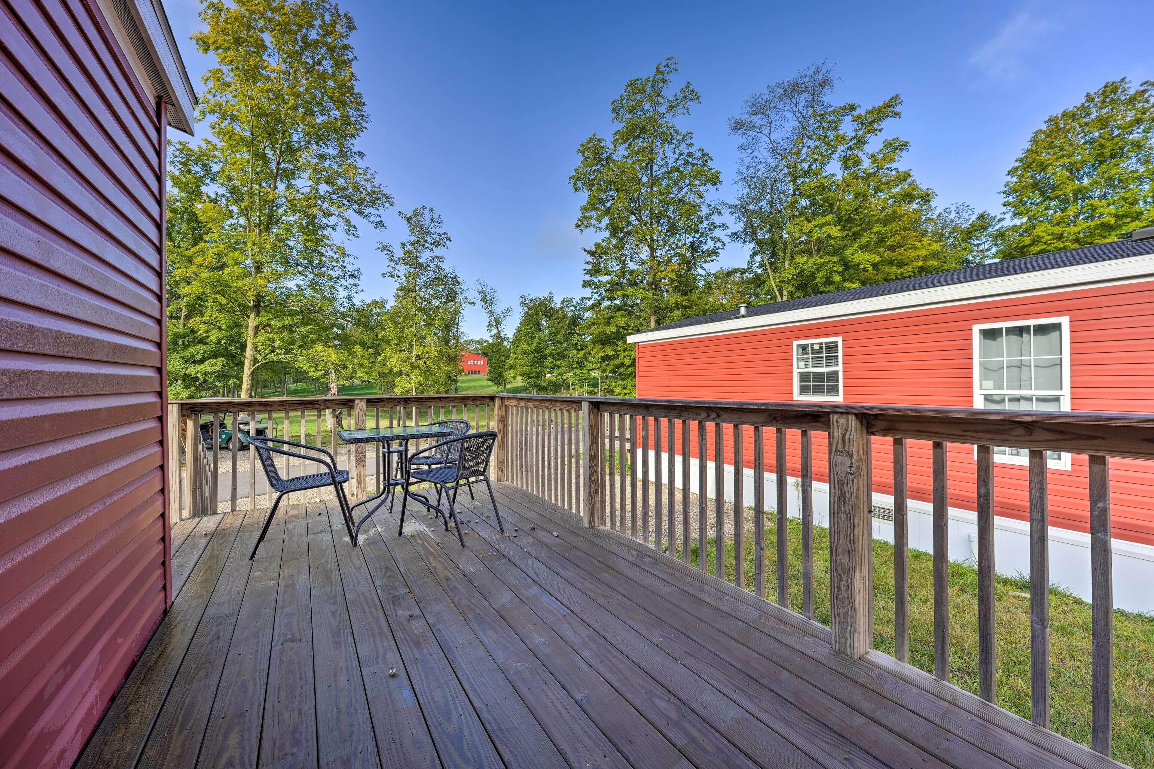 A wooden deck with a table and chairs, a red building, and trees in the background.
