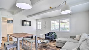 Ein modernes Wohnzimmer mit einem Holzesstisch, Metall-Barhocker, einem grauen Sofa und einem kleinen runden Couchtisch.