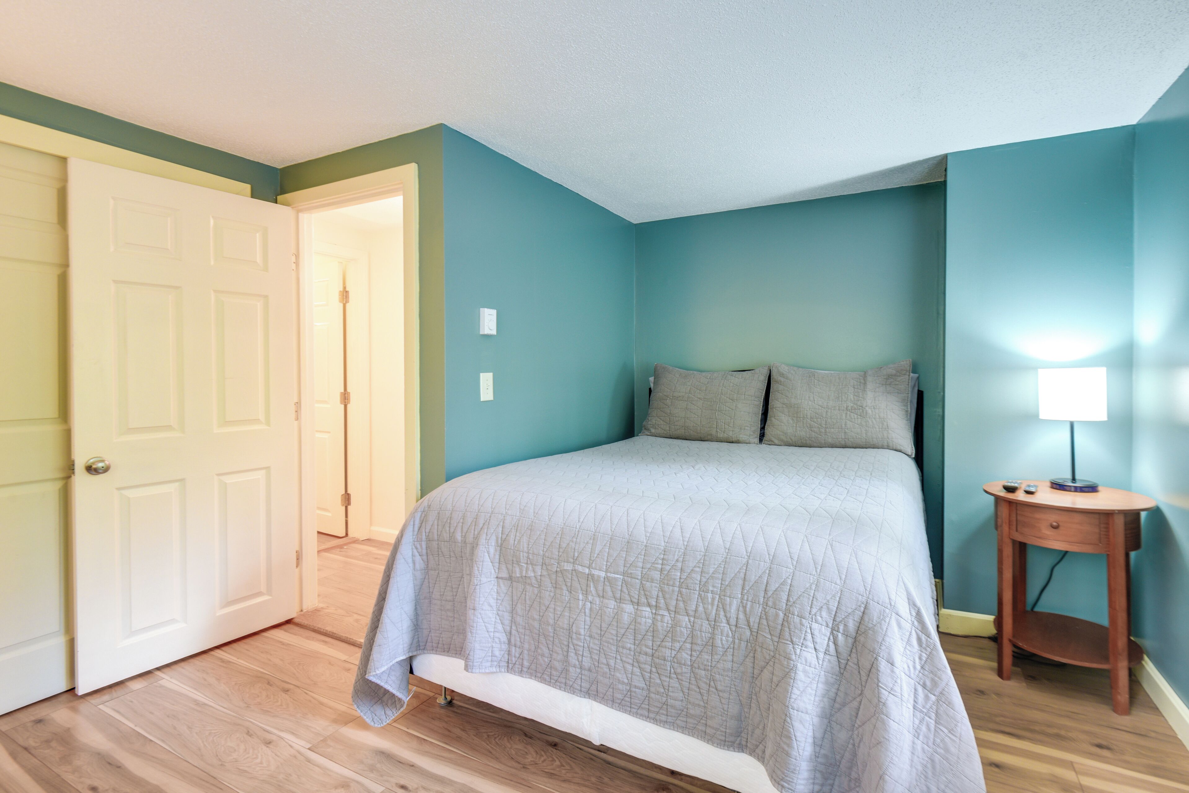 A bedroom with a bed, a nightstand, and a door leading to another room.