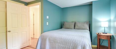 A bedroom with a bed, a nightstand, and a door leading to another room.