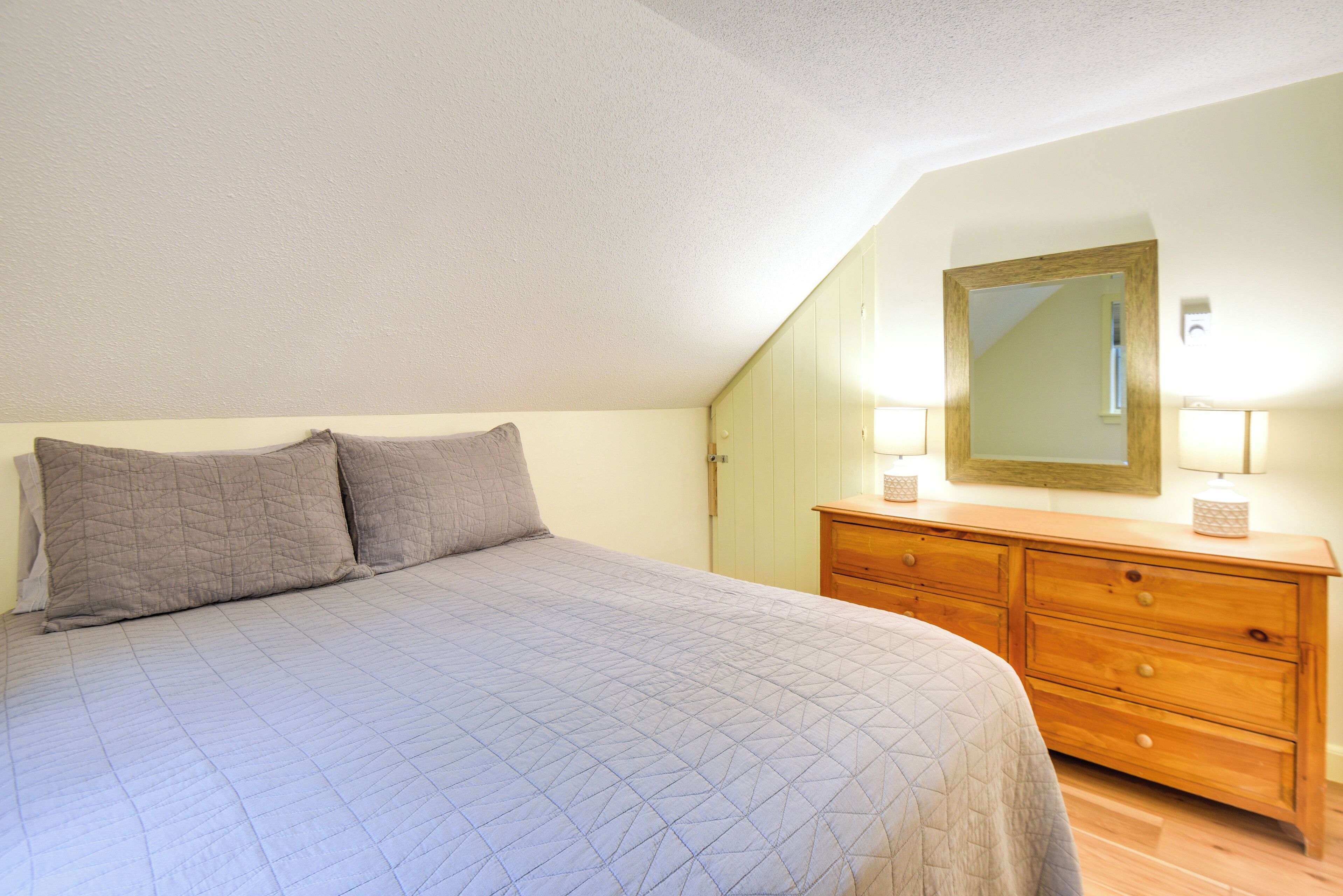 Un dormitorio con una cama, dos almohadas, un aparador de madera y un espejo.