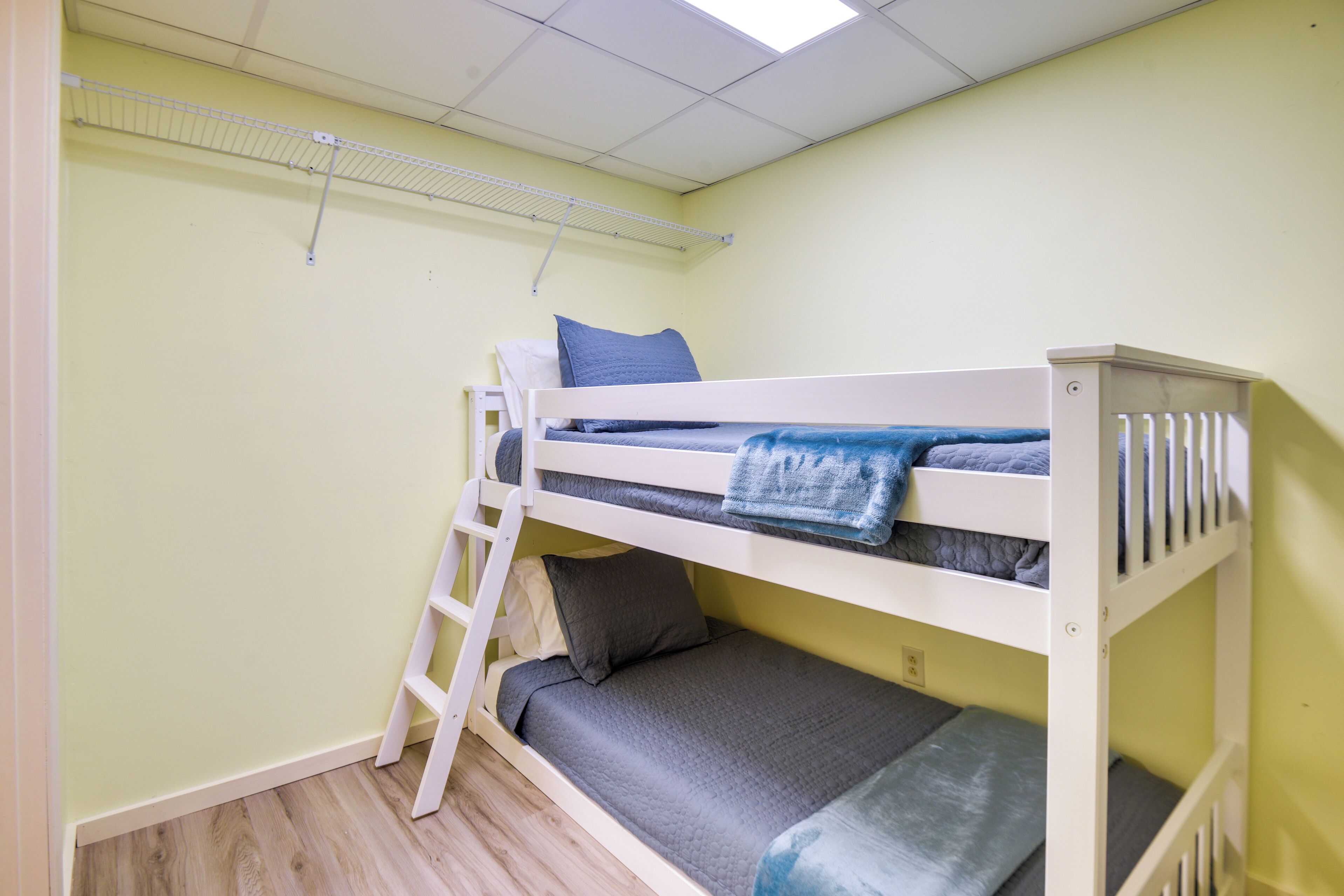 Een stapelbed met een ladder, een plank erboven en een effen muur.