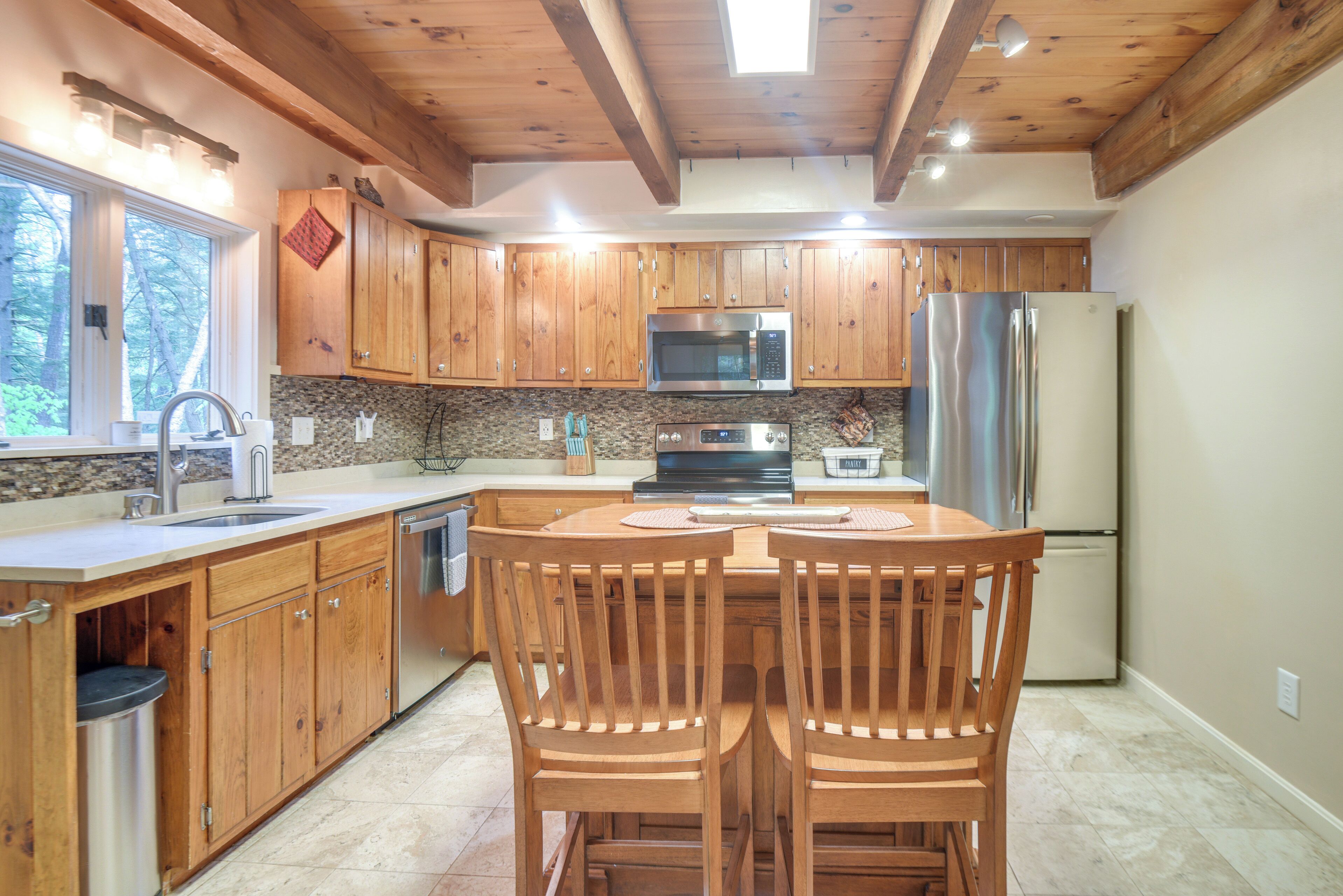 A kitchen with wooden cabinets, stainless steel appliances, and a dining area with two wooden chairs.