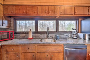 A kitchen with wooden cabinets, a granite countertop, a stainless steel sink, a red microwave, a blender, and a dishwasher. - Fire Pit & Grill: Lakefront Poconos Cottage! (East Stroudsburg)