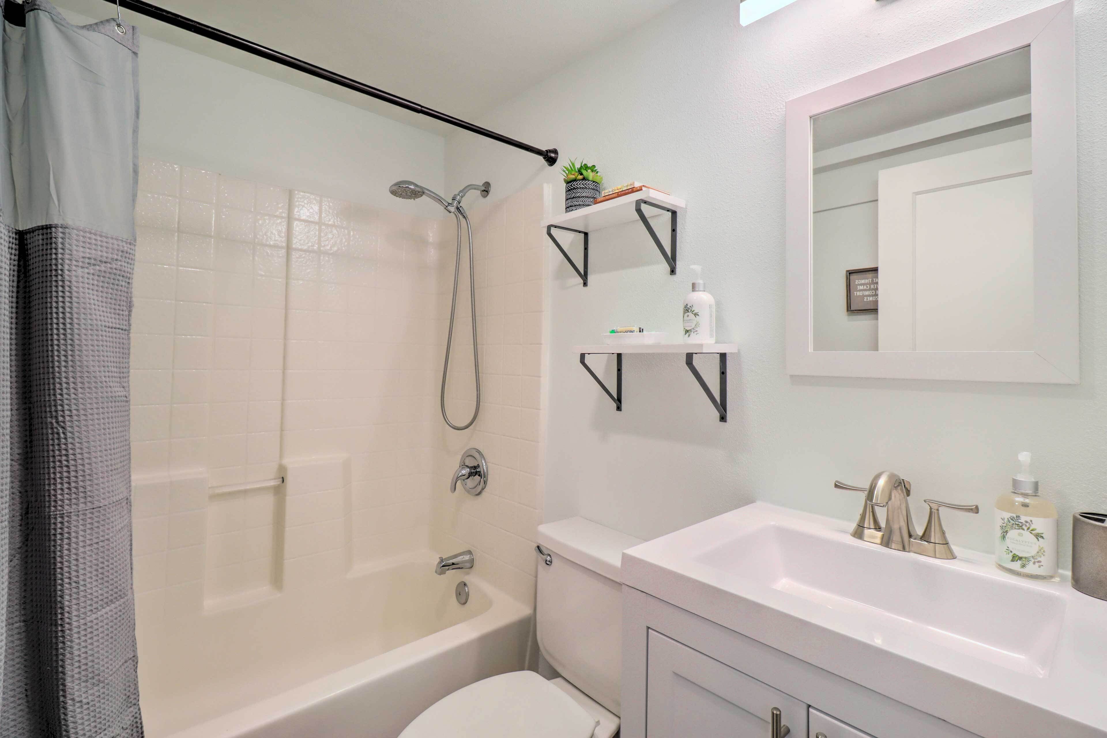 Une salle de bain moderne équipée d’une douche, de toilettes et d’un lavabo. On y trouve des étagères avec des articles de toilette et un miroir au-dessus du lavabo.