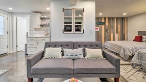 A modern living room with a grey sofa, a small table with a vase, and a kitchen in the background. - Ski & Hike: Cozy Dtwn Reno Studio w/ Fireplace (Reno)