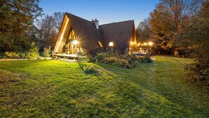 Une maison moderne avec un toit en pente, entourée d’une pelouse bien entretenue et d’arbres.