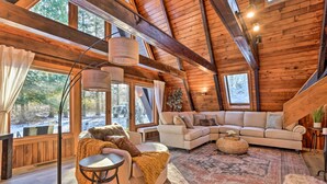 L’intérieur d’un chalet chaleureux, avec une grande fenêtre, une table ronde, un canapé et un tapis.