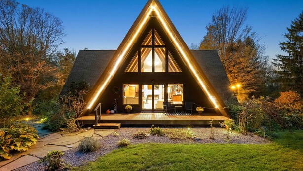 Une maison moderne avec un toit triangulaire, de grandes fenêtres et une véranda bien éclairée.