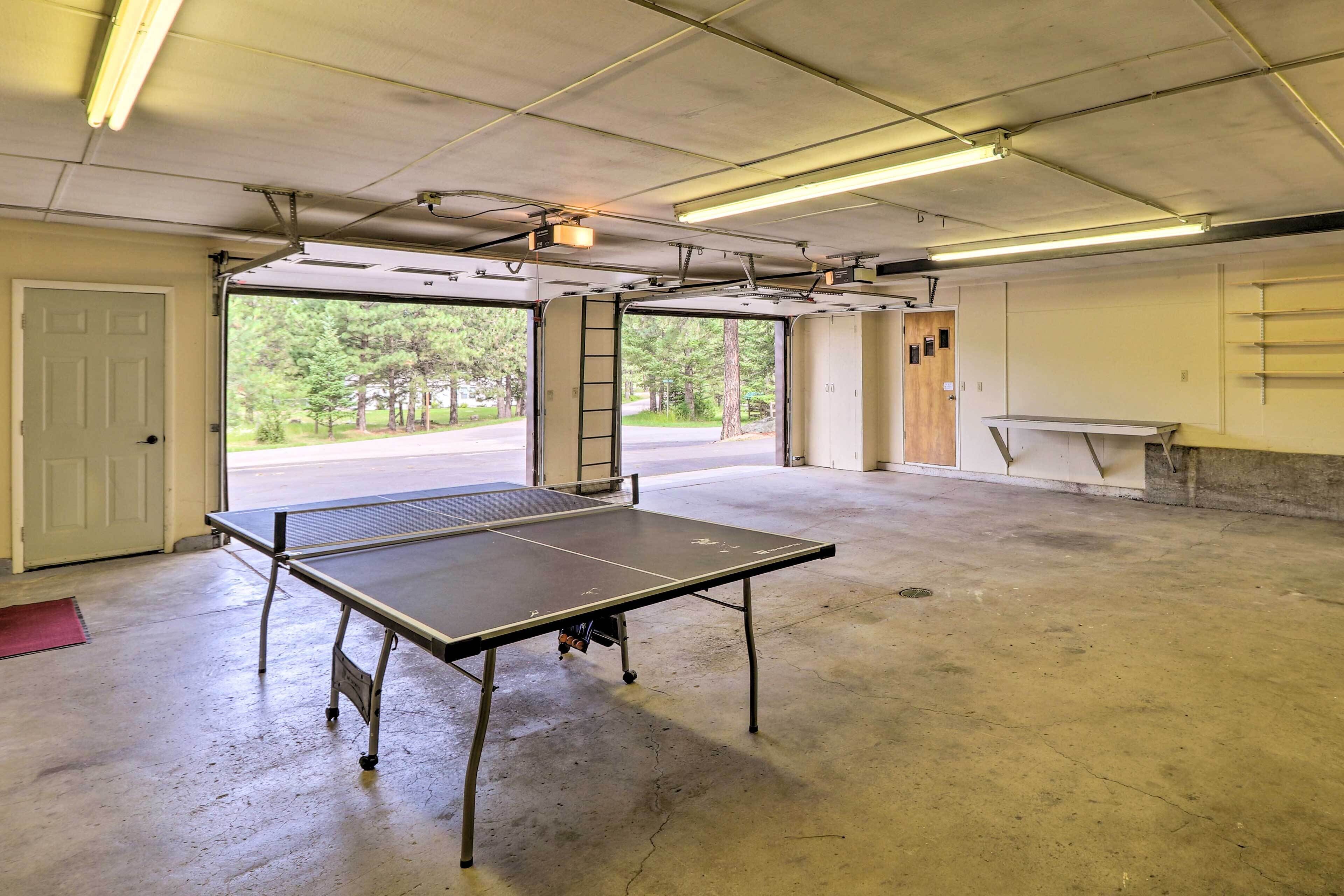 A spacious indoor area with a ping pong table, concrete flooring, and large windows offering a view of trees and a road.