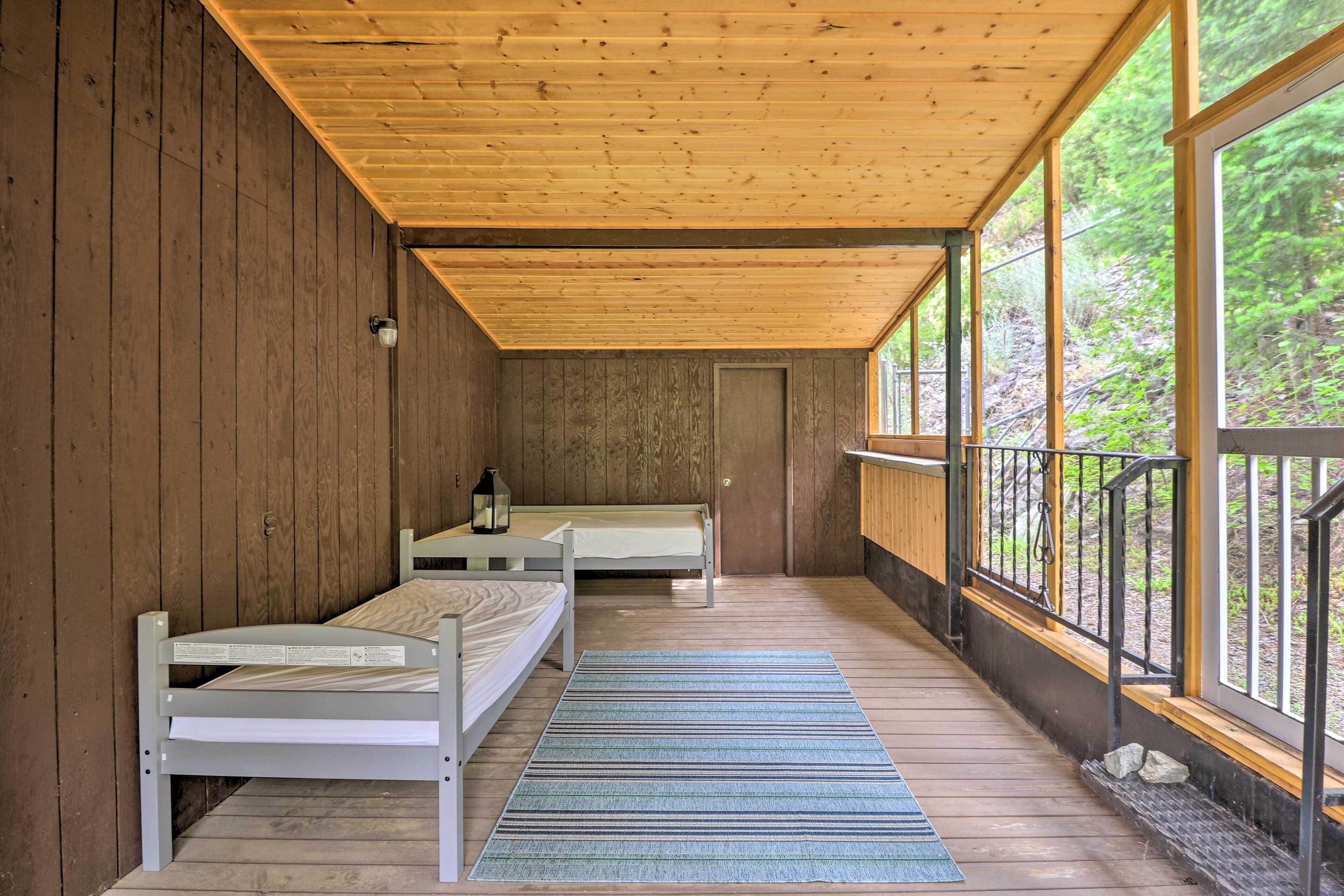 A cabin with two wooden beds, a wooden ceiling, and large windows offering a view of the forest.
