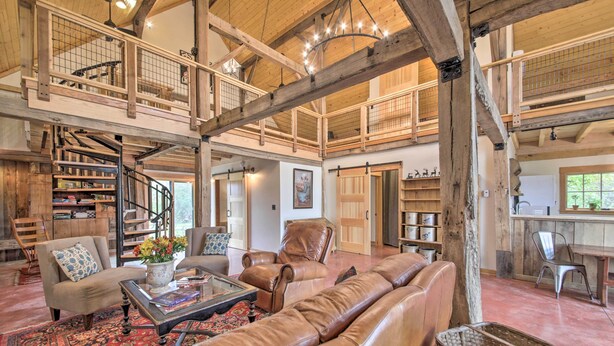 Ein großzügiger Wohnbereich mit hoher Decke, Holzbalken, einer Wendeltreppe, Ledersofas, einem Couchtisch und einem großen Fenster.