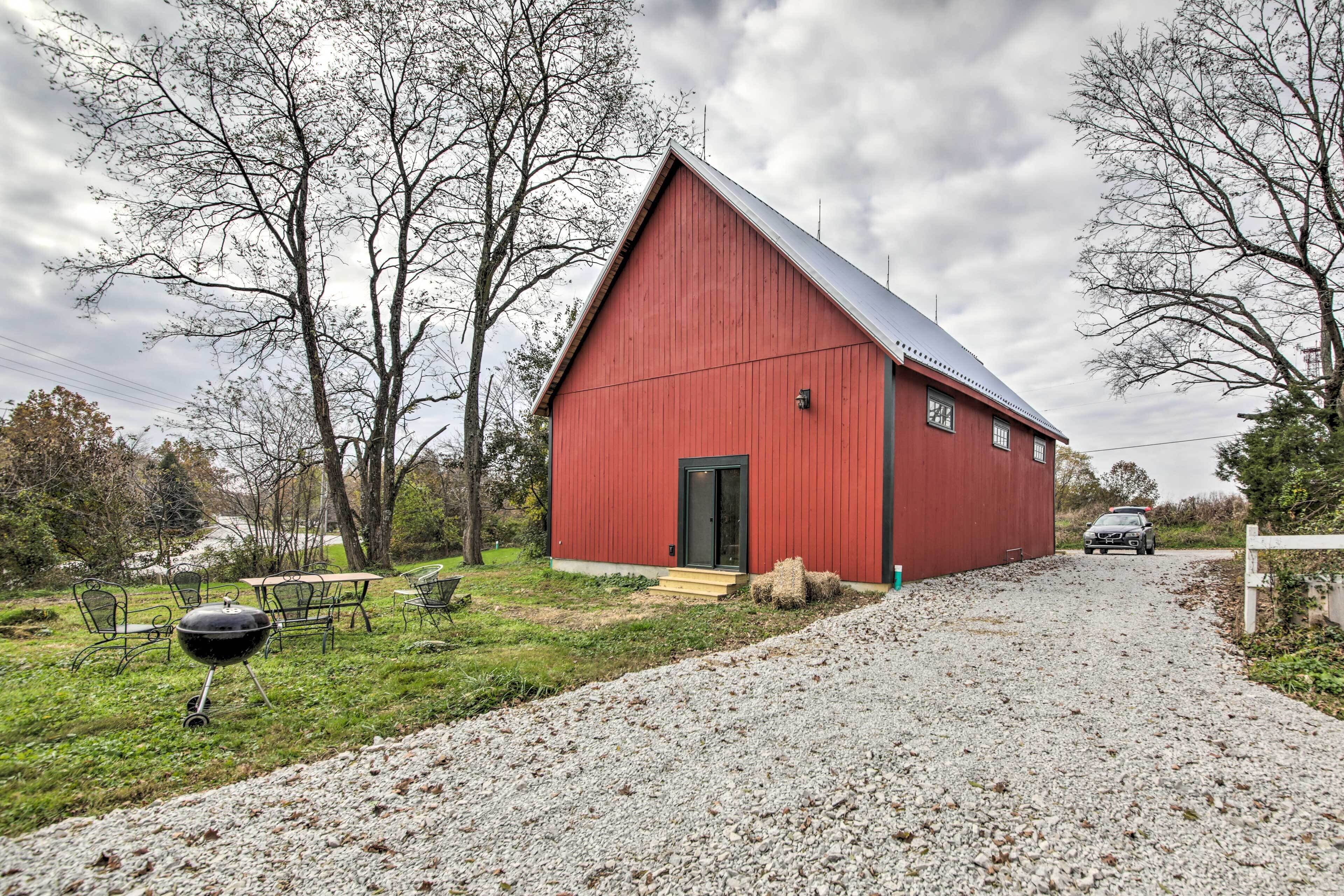 A red barn with a gravel driveway leading to it, surrounded by trees and a picnic table.