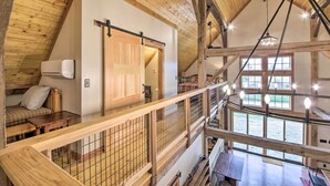 Ein Zimmer mit hohen Decken, Holzbalken, einem Bett, einem Schreibtisch und Blick ins Freie durch große Fenster.
