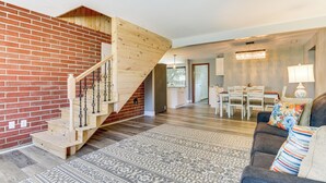 A spacious living area with a wooden staircase, a patterned rug, and a sofa with colorful cushions. - Indian Lake Vacation Rental w/ Fire Pit & Sauna (Lakeview)