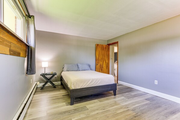 A bedroom with a bed, bedside table, and a window with curtains. - Indian Lake Vacation Rental w/ Fire Pit & Sauna (Lakeview)