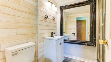 A bathroom with wooden panel walls, a white toilet, a pedestal sink, and a large ornate mirror.