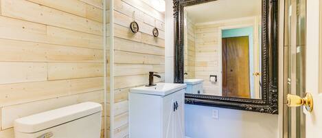 A bathroom with wooden panel walls, a white toilet, a pedestal sink, and a large ornate mirror.