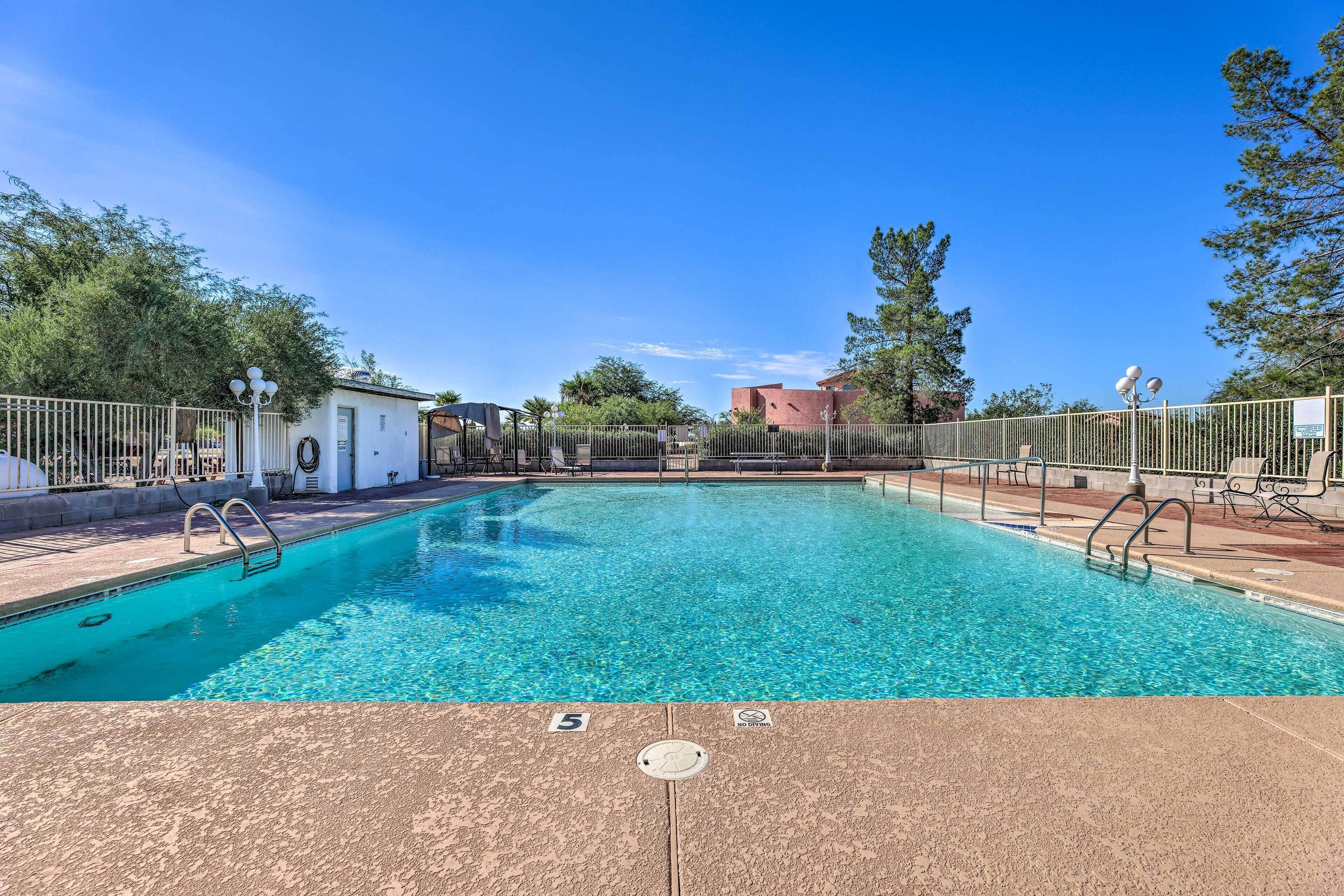 A clear swimming pool with a tiled deck, surrounded by a fence, and a building in the background.