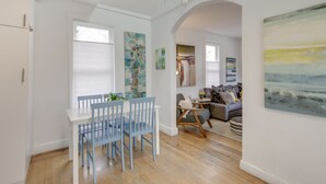 Ein Essbereich mit einem weißen Tisch und blauen Stühlen, ein Wohnzimmer mit einem grauen Sofa und einem Gemälde sowie ein Flur mit Holzboden und weißen Wänden.