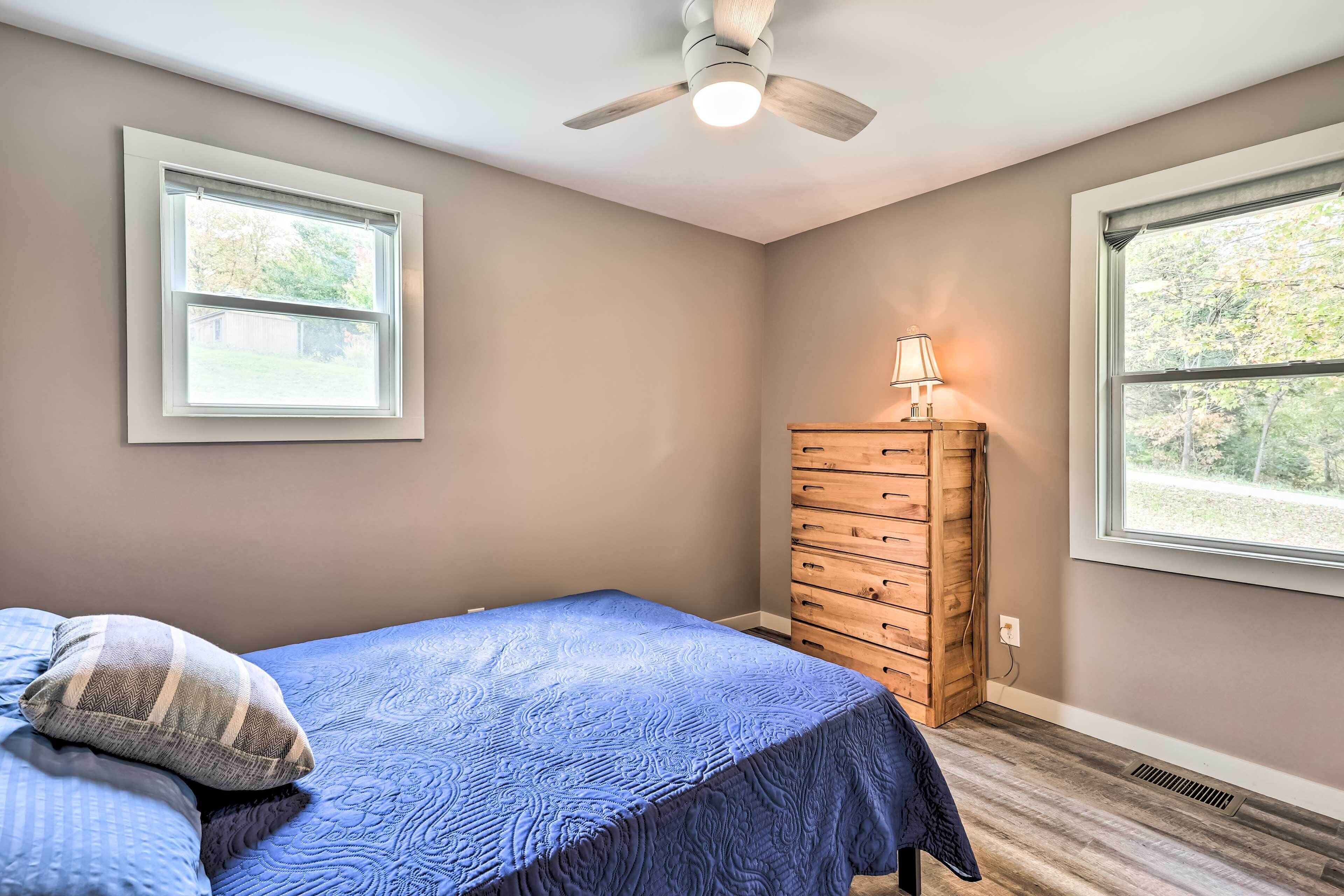 Un dormitorio con cama, cómoda, dos ventanas y ventilador de techo.