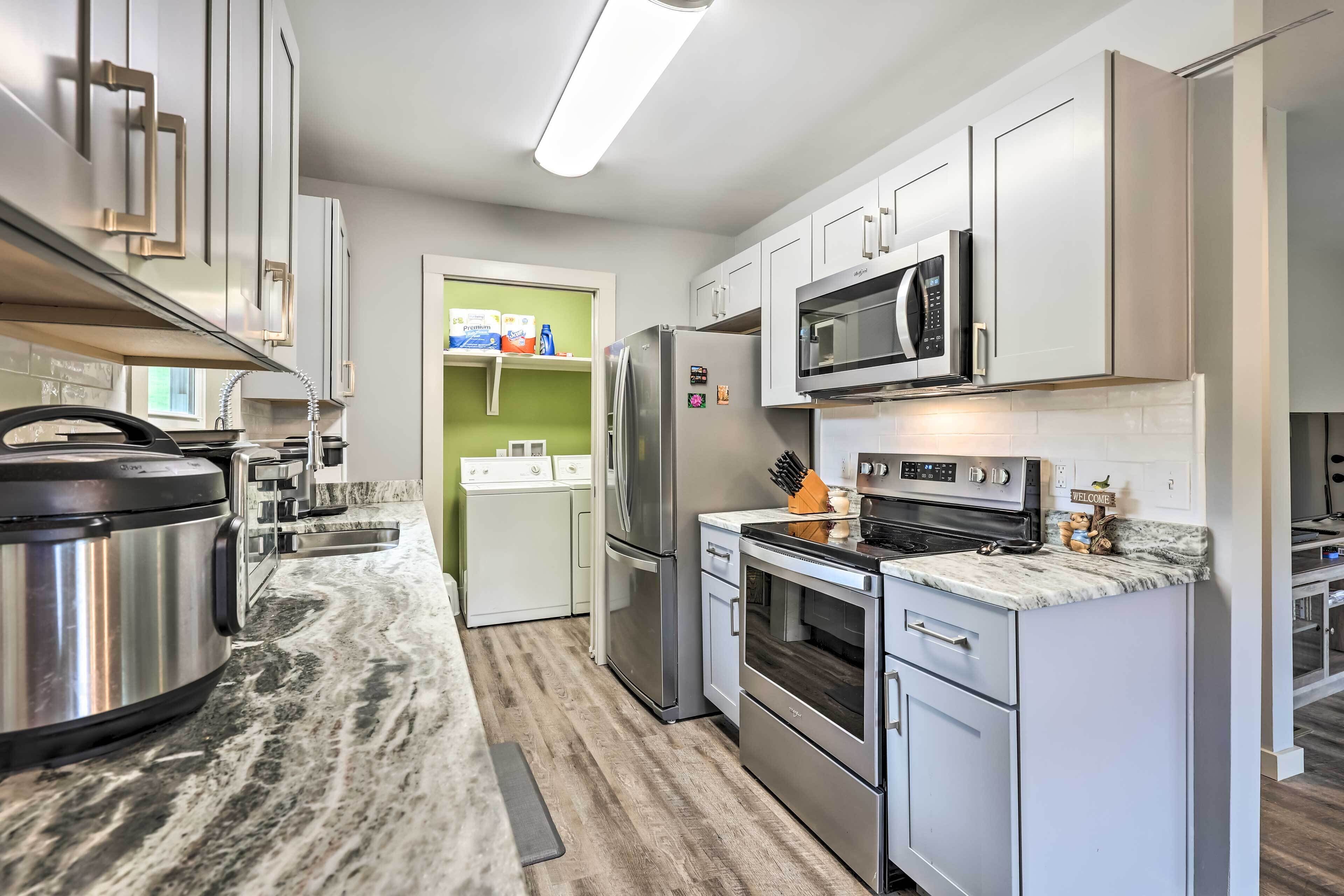 A modern kitchen with stainless steel appliances, white cabinetry, and a marble countertop.