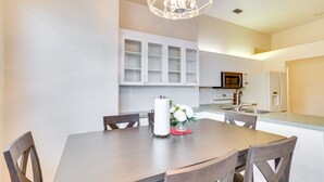 A modern kitchen with white cabinets, a microwave, and a refrigerator. There is a dining table with chairs and a vase with flowers. - Port St Lucie Home ~ 3 Mi to Botanical Gardens! (Port Saint Lucie)
