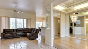 A spacious living room with a sectional sofa, a ceiling fan, and a large window with curtains. - Port St Lucie Home ~ 3 Mi to Botanical Gardens! (Port Saint Lucie)