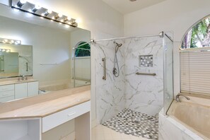 A modern bathroom with a glass-enclosed shower, a large mirror with lights, and a bathtub.