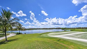 Un campo de golf con un cuerpo de agua, palmeras y un cielo despejado.