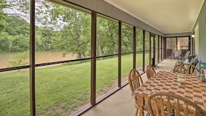 A covered patio with a table and chairs, large windows offering a view of a grassy area and trees. - Norfork Getaway: Walk in White River Access! (Norfork)