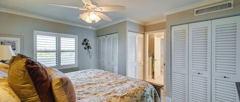 A bedroom with a bed, a ceiling fan, white shutters, and a closet.