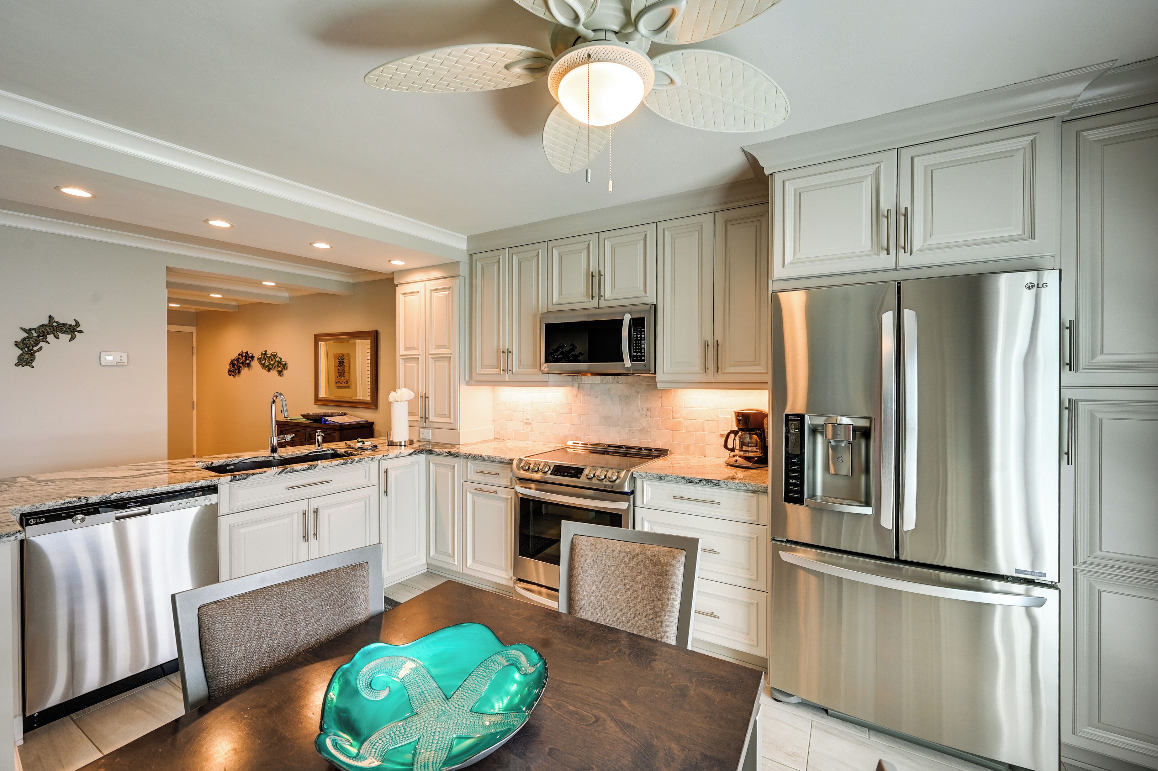 A modern kitchen with white cabinetry, stainless steel appliances, and a ceiling fan.